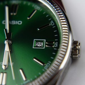 Close-up of a sleek green dial wristwatch highlighting time and date features.