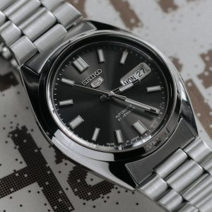 Close-up of a Seiko automatic watch with a metal band on printed text background.