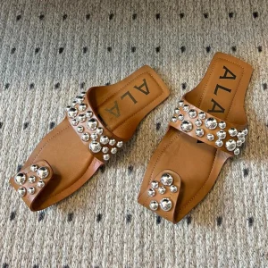 ALAIA FOLDED FLAT MULES WITH SPHERES ON COPPER BROWN CALFSKIN